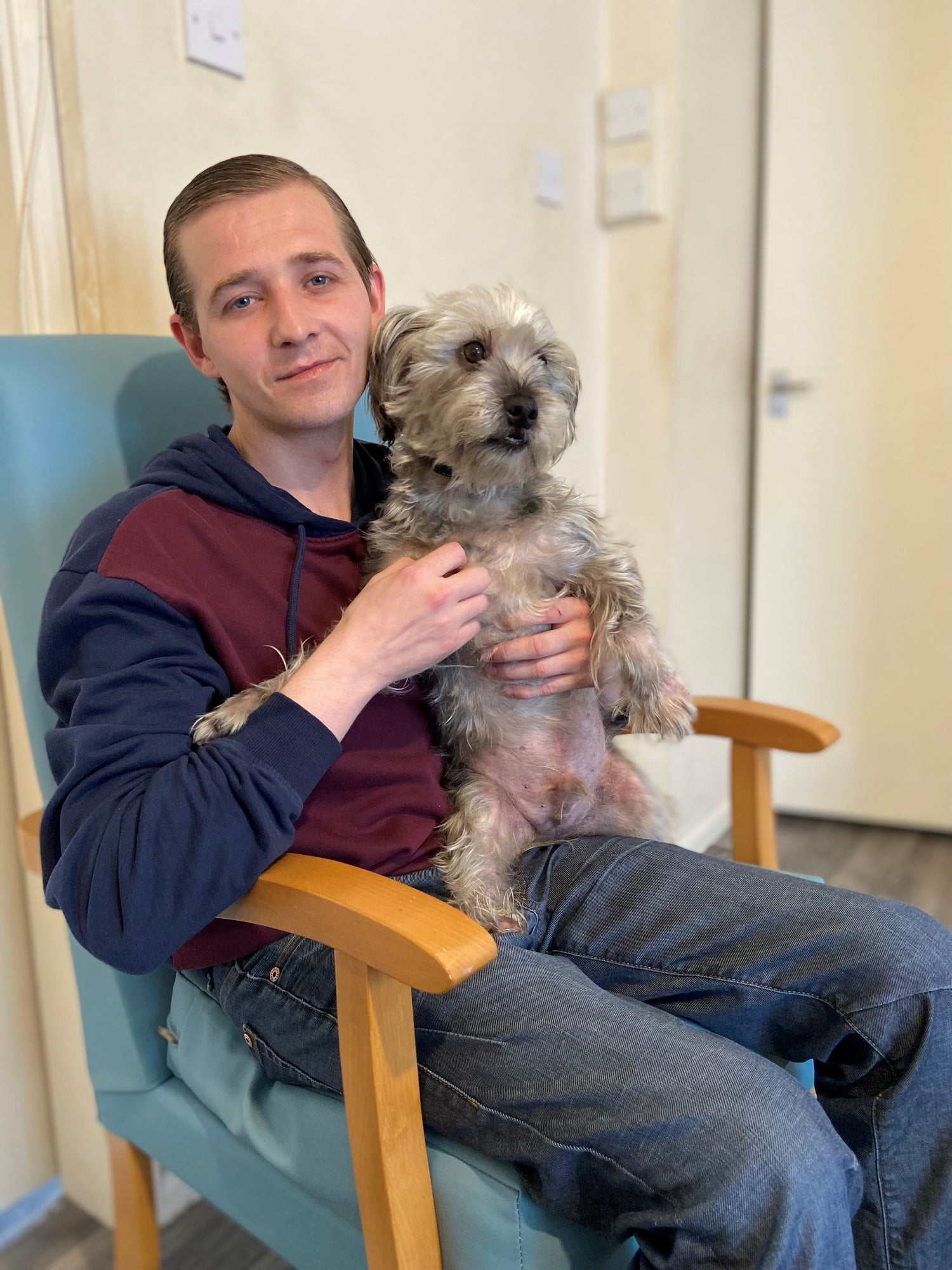 Man sat in a chair smiling holding a dog.