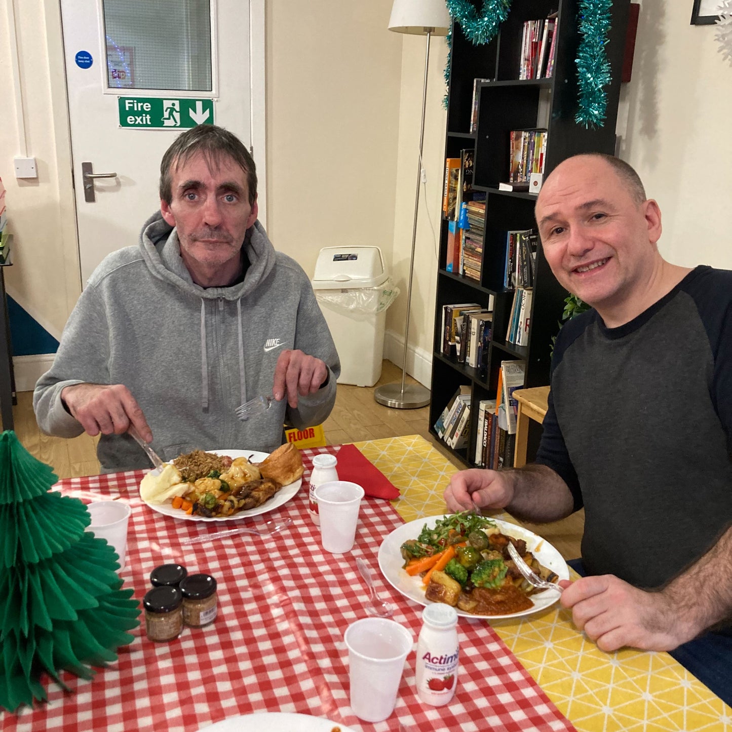 Two men sat enjoying their Christmas dinner smiling at the camera.
