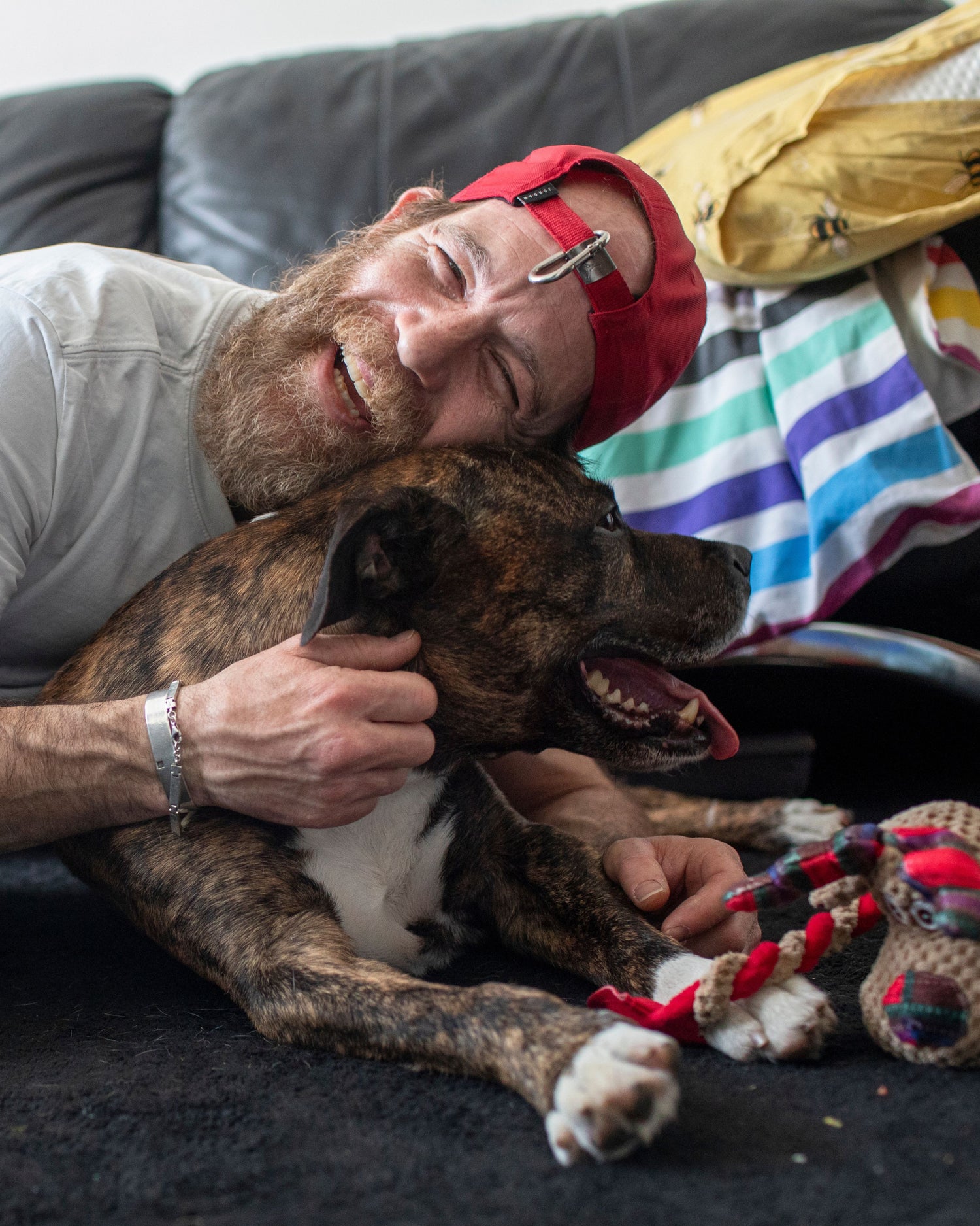 Man lying on a couch with a dog, both looking happy and relaxed.