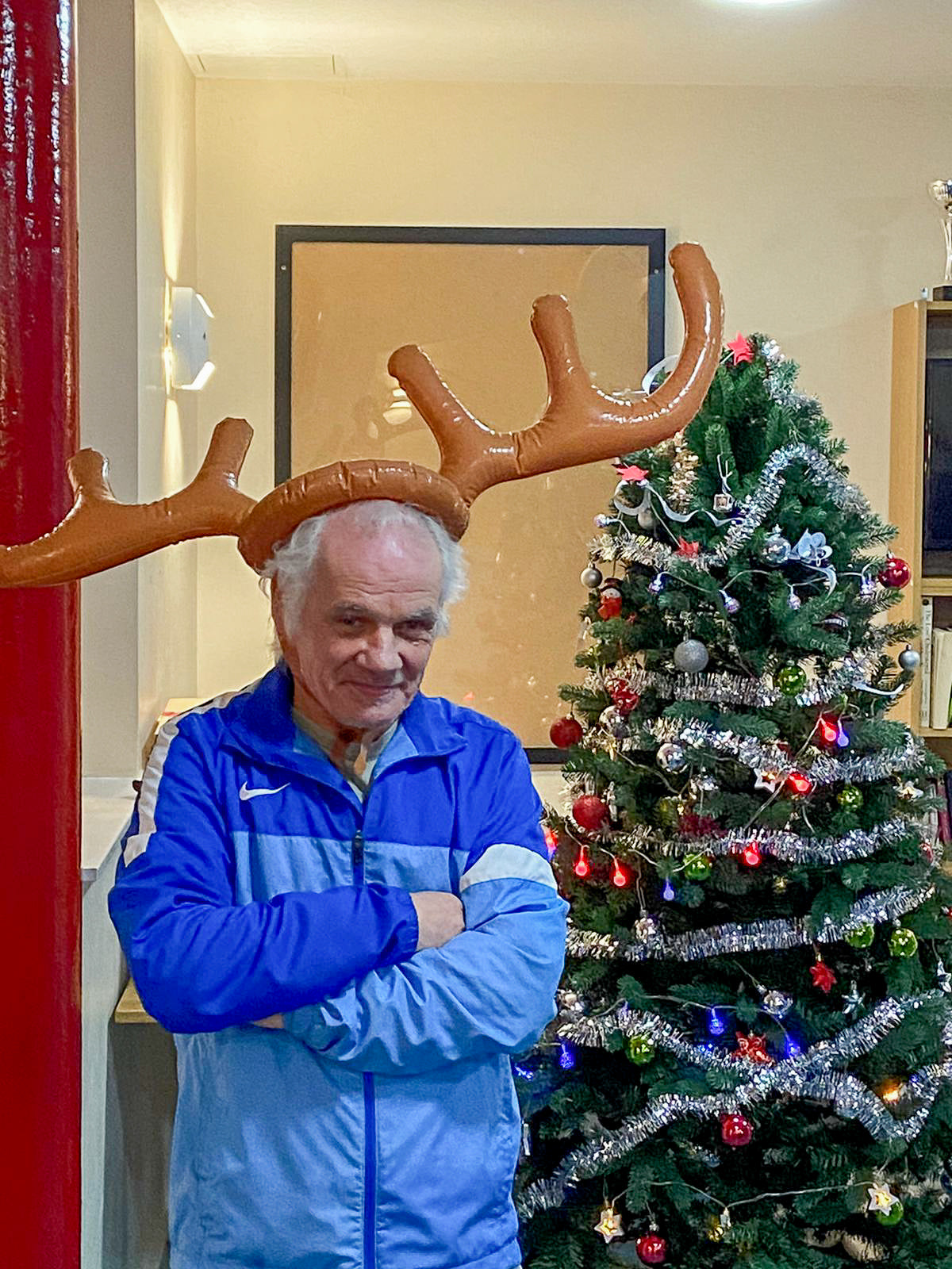 Man with antlers on his head stood next to a Christmas tree.