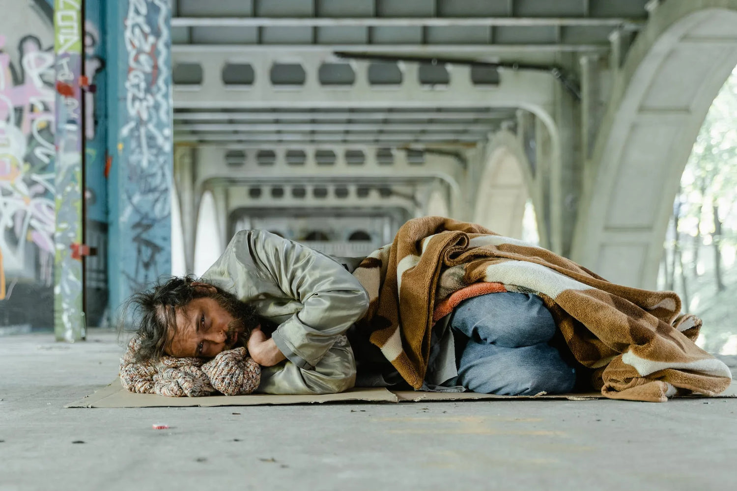 Man rough sleeping under a bridge looking towards the camera.