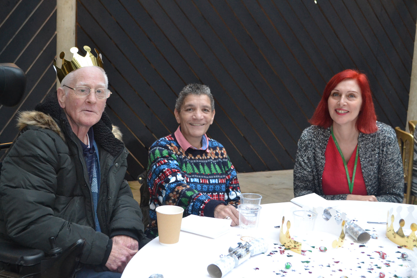 Three people sat at a table with Christmas crackers and gold crowns.