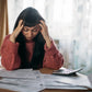 Woman looking distressed sat at a table with papers and a calculator.