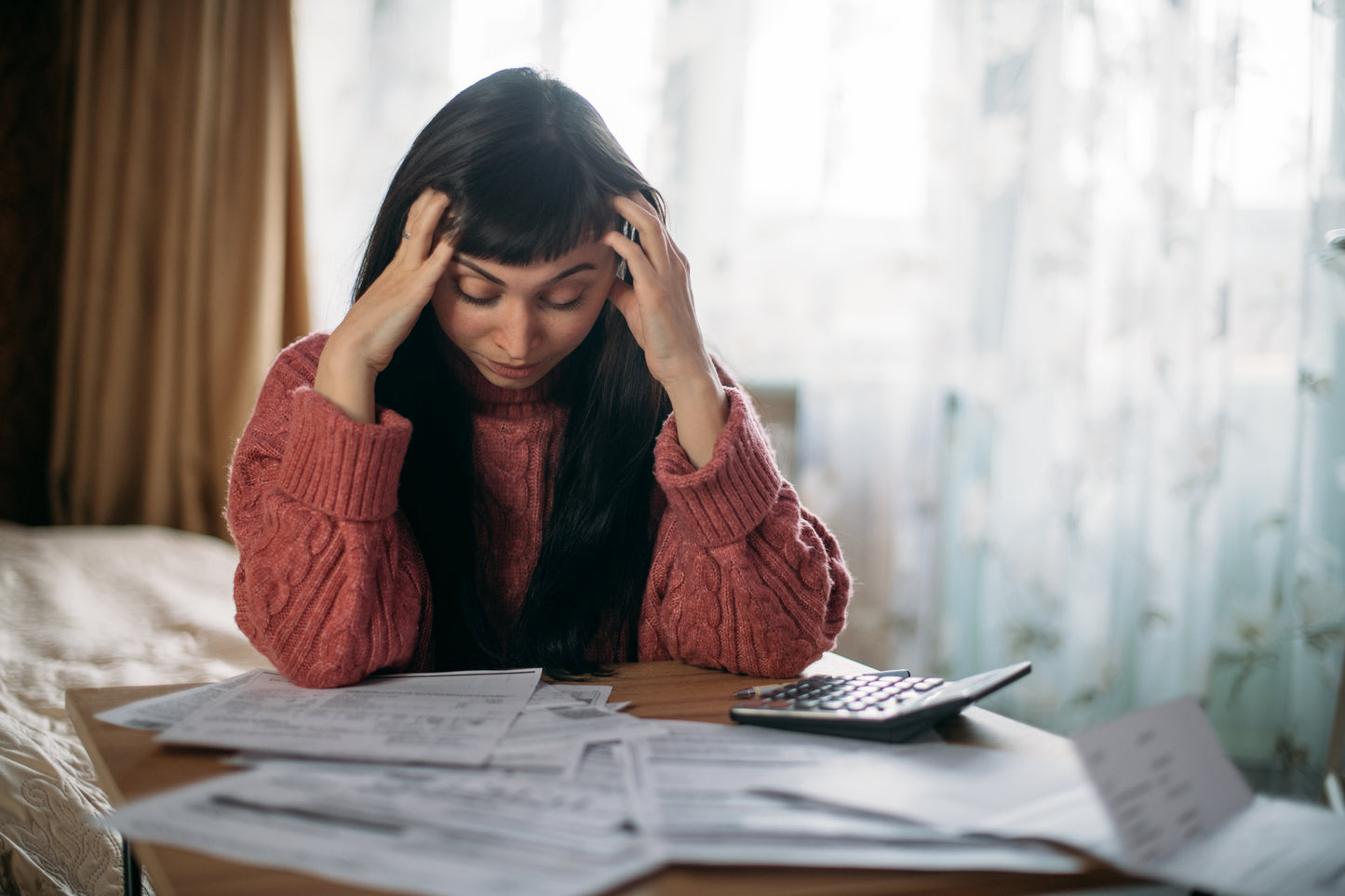 Woman looking distressed sat at a table with papers and a calculator.